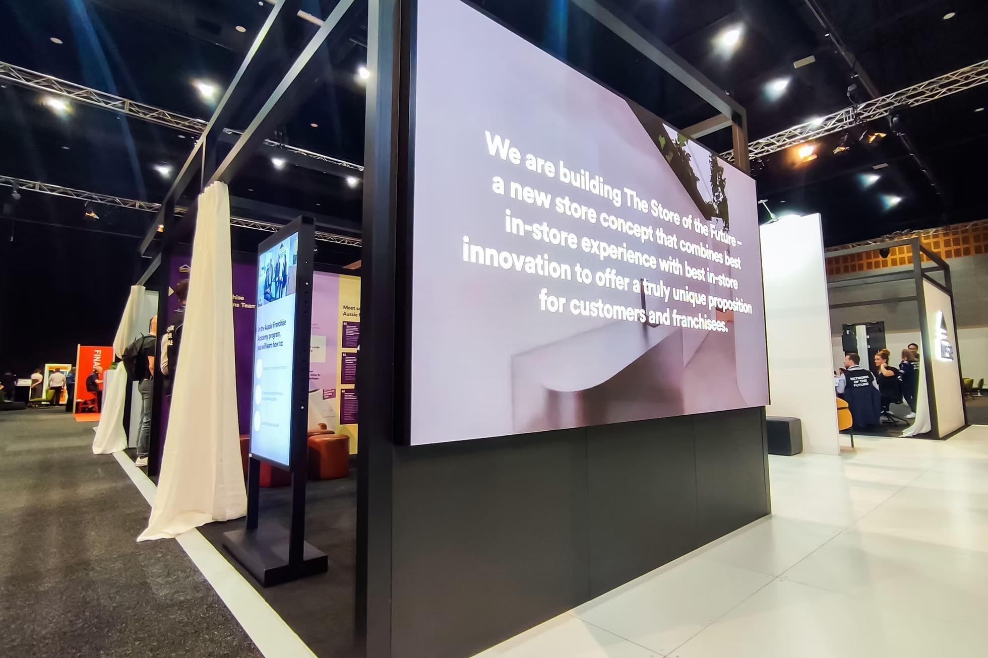 Large LED display at a franchise expo showcasing text about future in-store concepts and innovations.