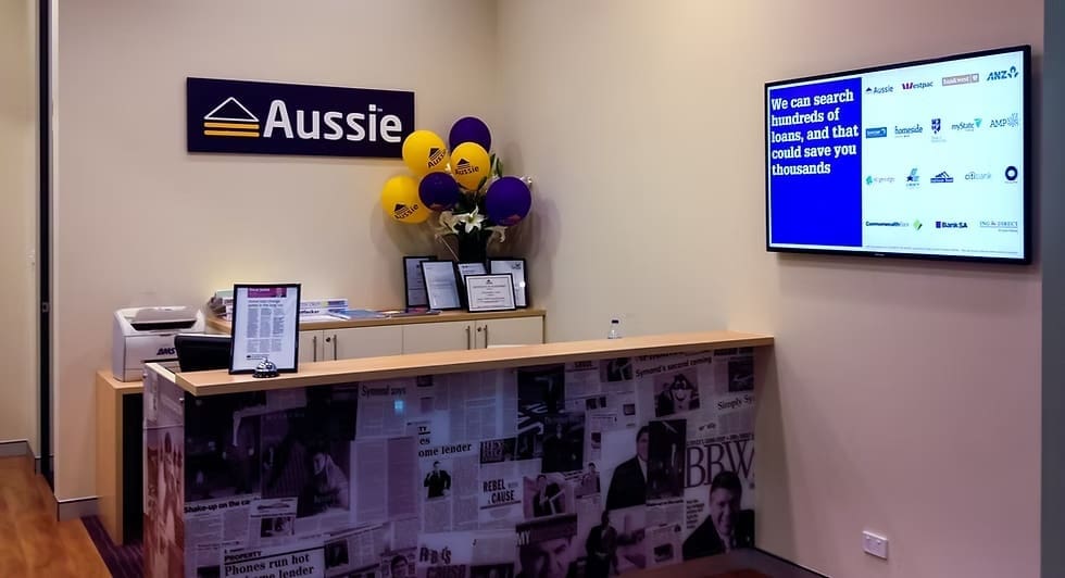 Interior of Aussie Home Loans branch featuring a digital display promoting loan comparisons and financial products.