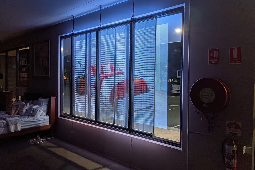 Transparent LED window display at Forty Winks showcasing bedroom furniture and decor under blue lighting.