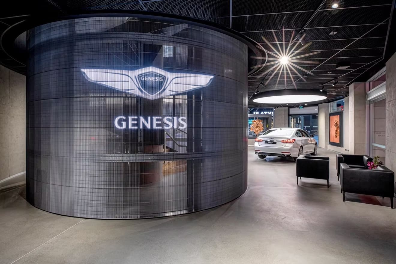 Genesis showroom with curved transparent LED display featuring brand logo and luxury car interior.