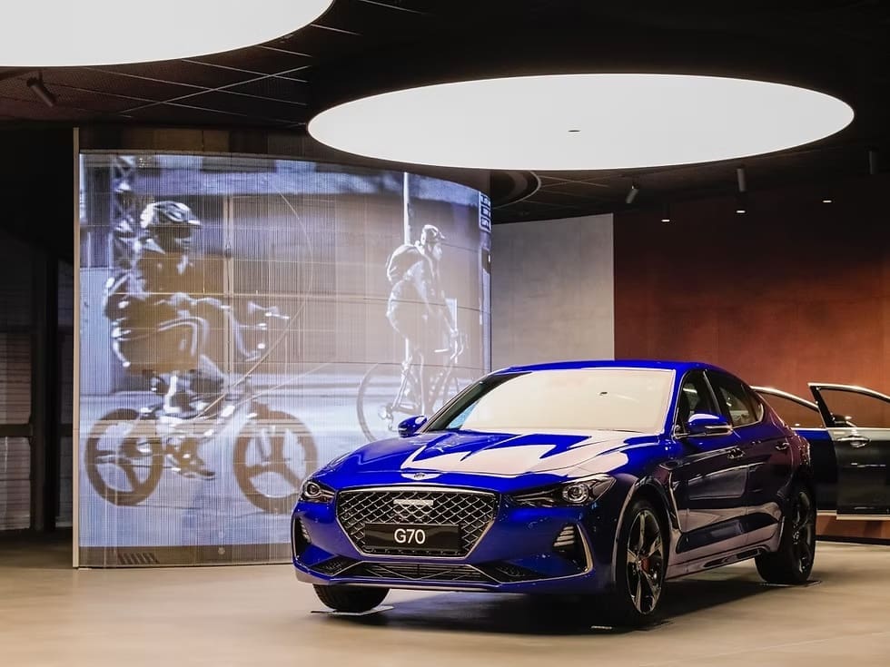 Blue Genesis G70 showcased in luxury showroom with LED backdrop and circular ceiling lighting.