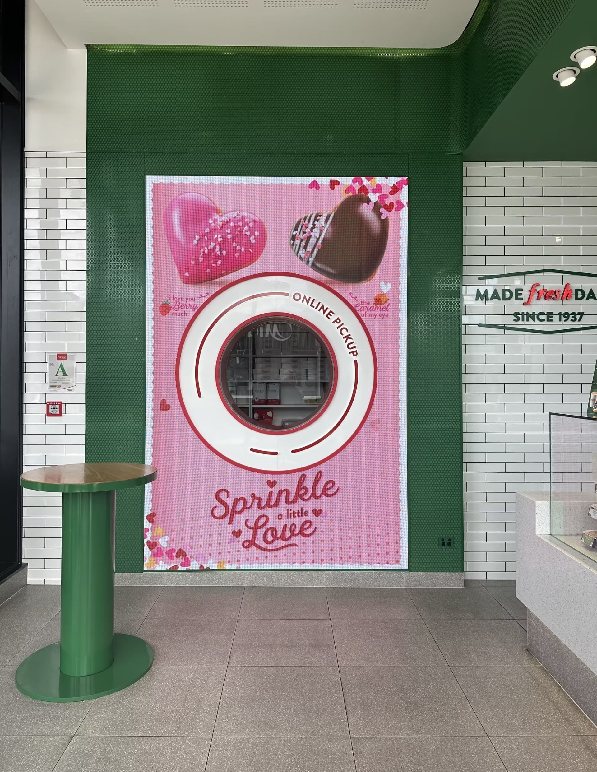 LED display wall at Krispy Kreme store featuring a Valentine’s-themed design with heart-shaped donuts and “Sprinkle a little Love” text.