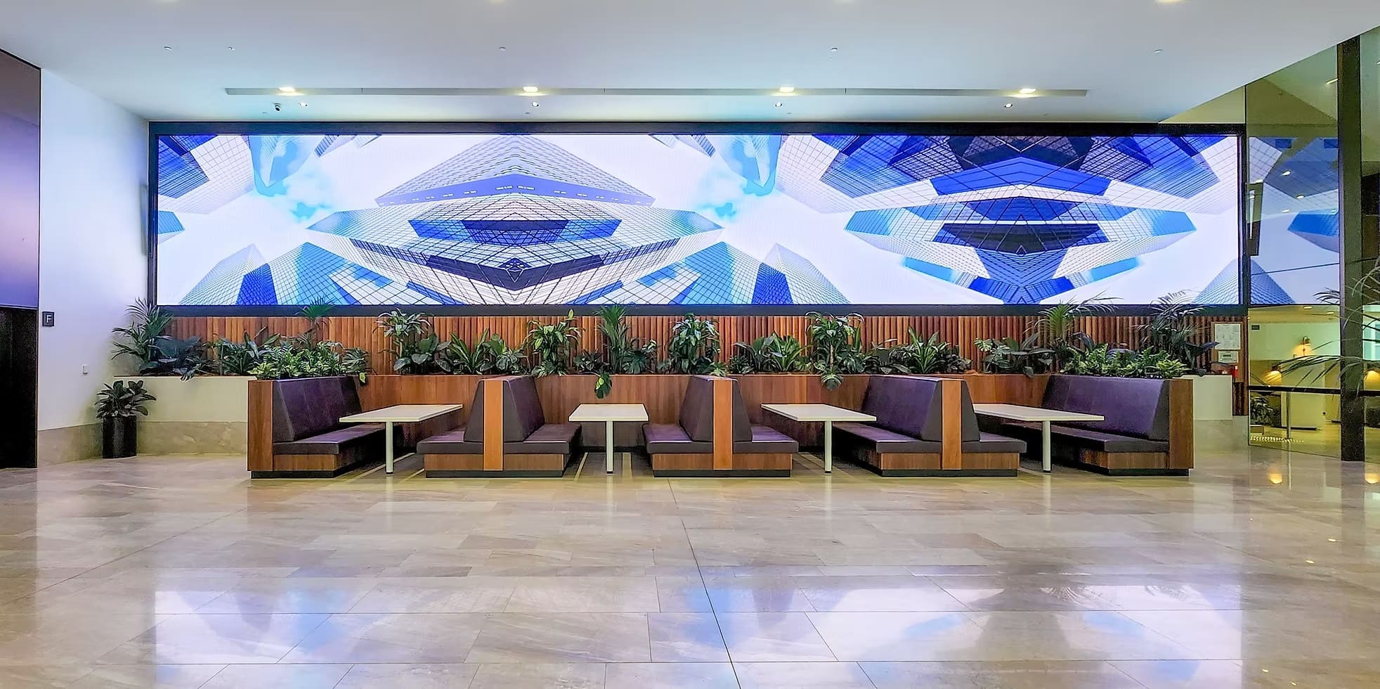 Indoor lounge area featuring a large panoramic LED display wall showing abstract cityscape visuals above booth seating.