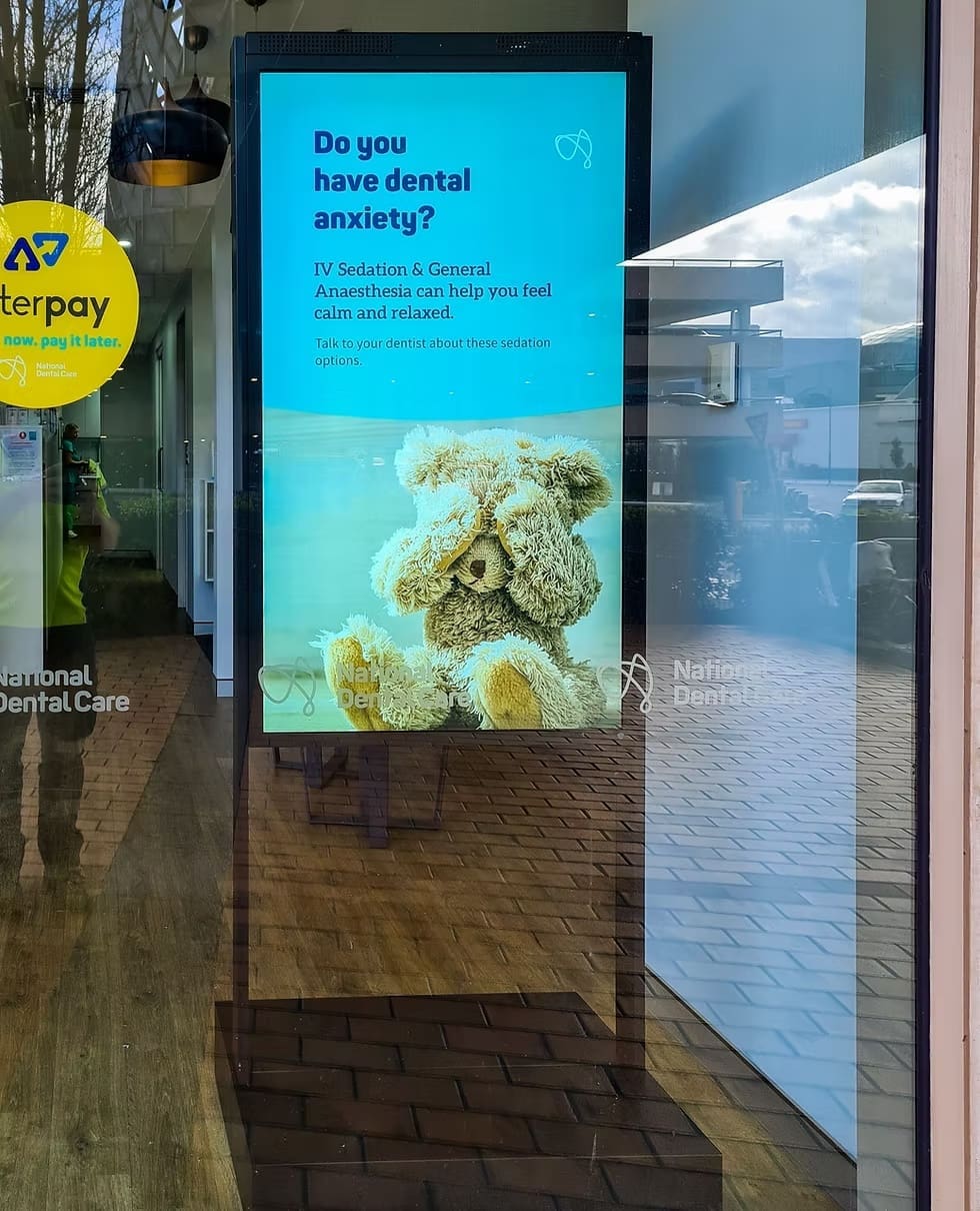 LED display outside National Dental Care clinic showing advertisement about IV sedation and dental anxiety relief with a teddy bear image.
