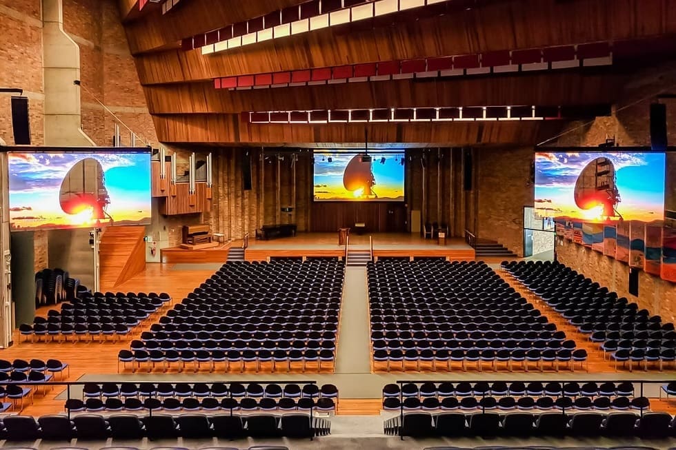Large indoor LED screens at the University of Newcastle auditorium displaying high-resolution visuals during an event setup.