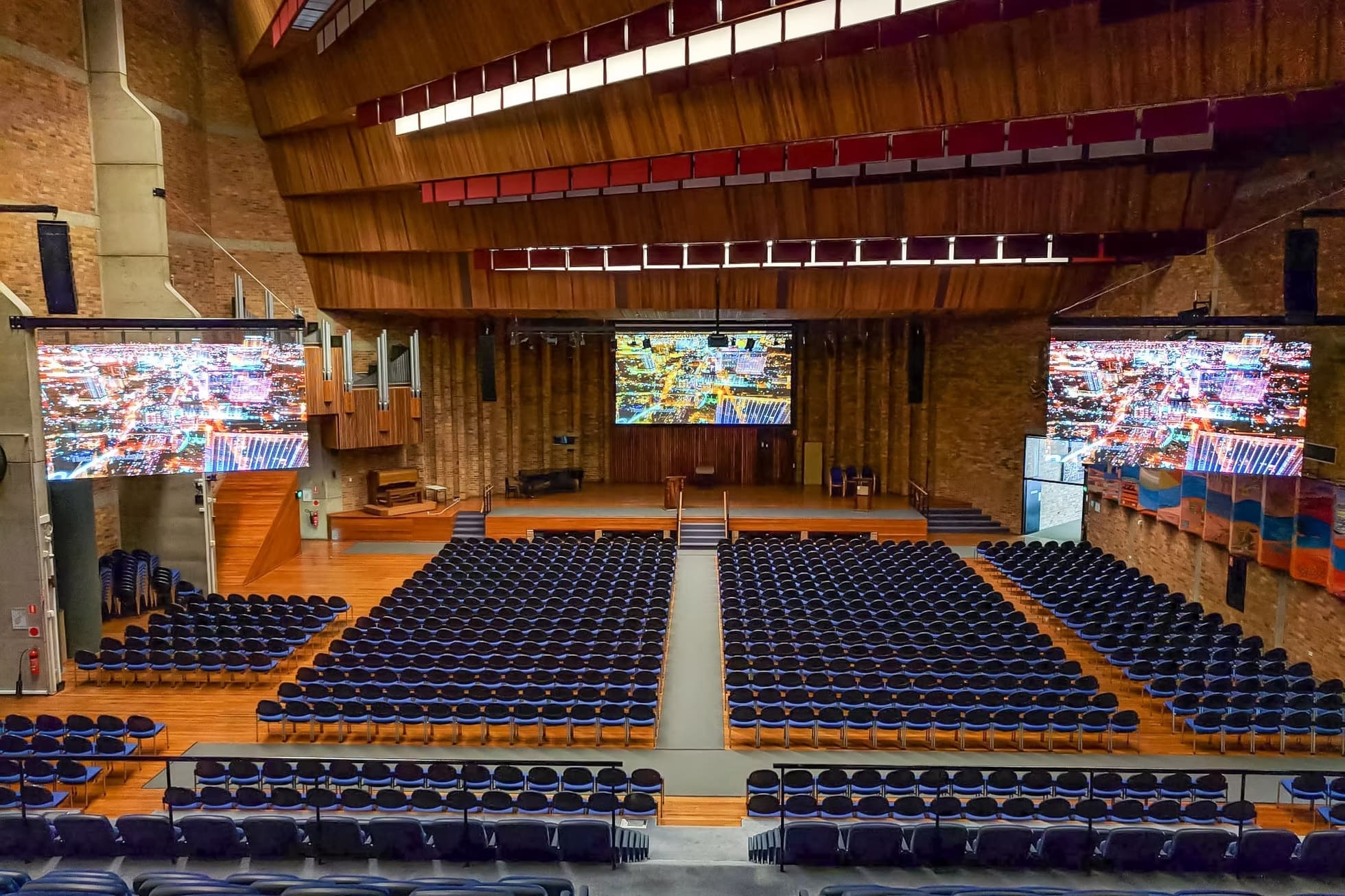 Auditorium with multiple LED screens displaying cityscape visuals at the University of Newcastle event hall.
