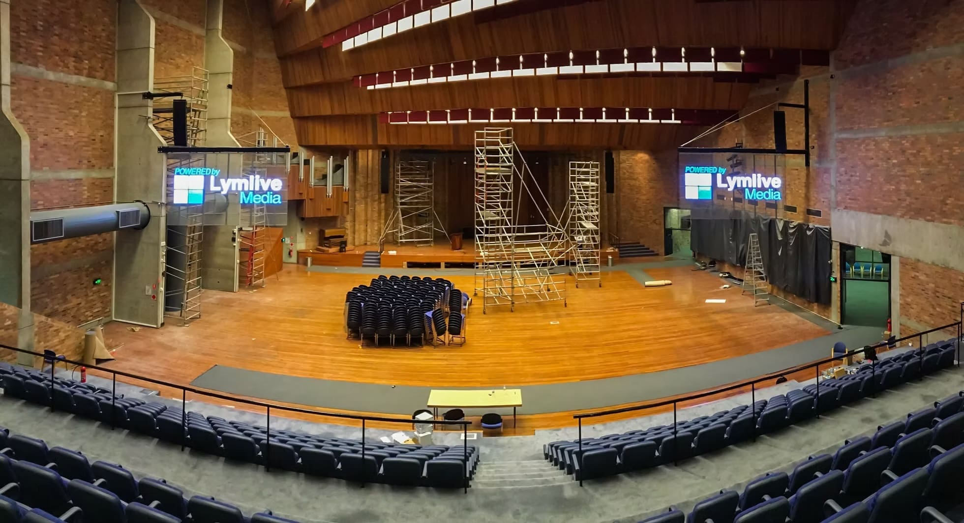Auditorium under setup with scaffolding and LED screens displaying “Powered by Lymlive Media.”