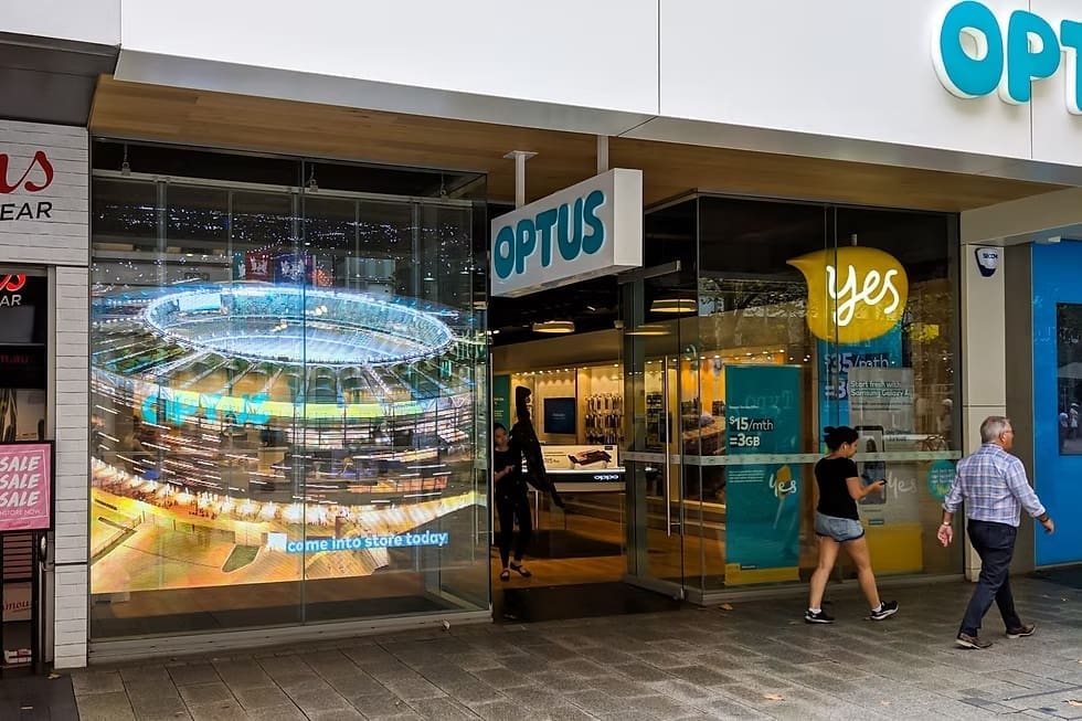 Optus storefront featuring large transparent LED screen displaying a stadium visual promoting Optus services.