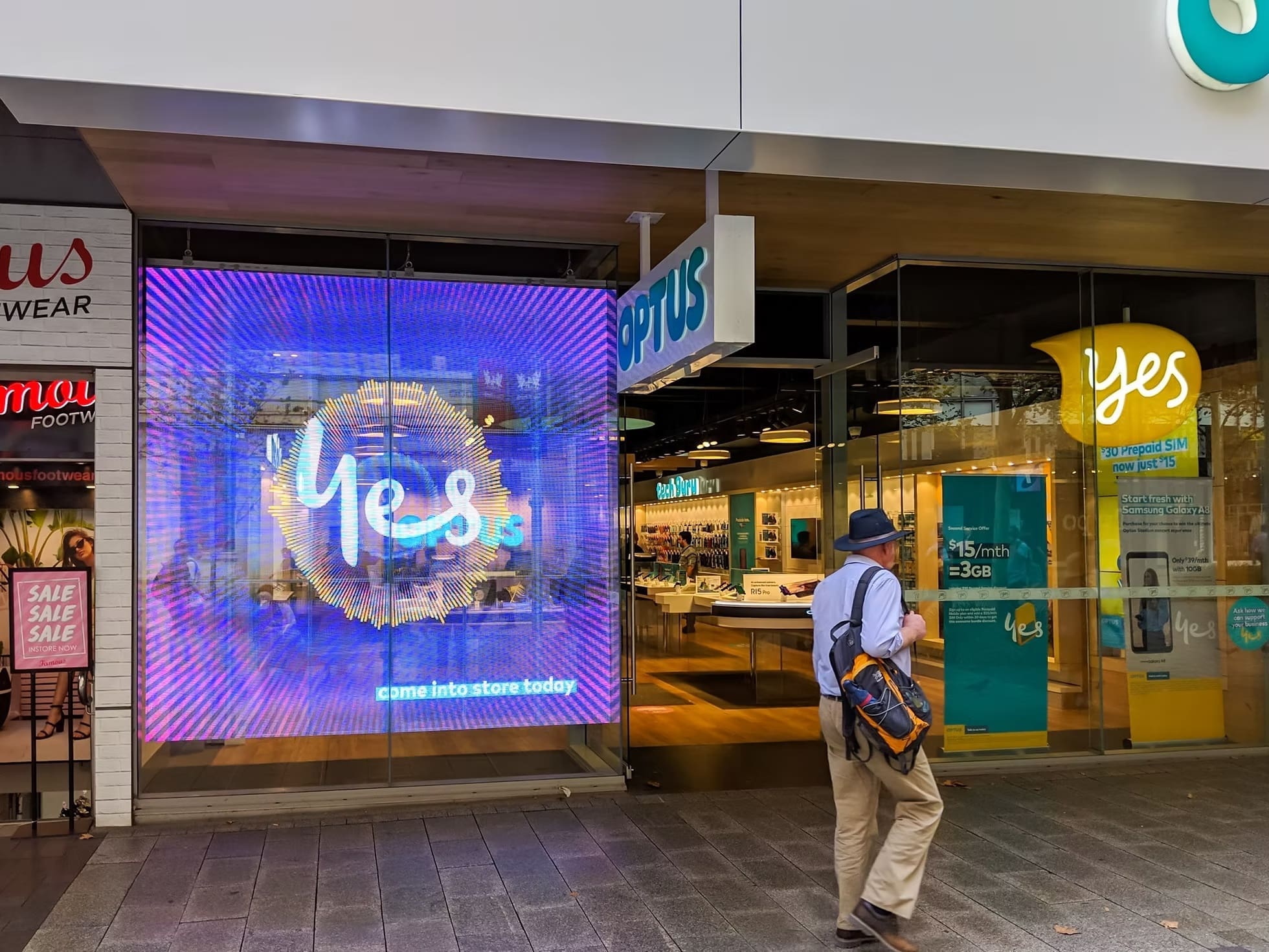 Optus storefront with large LED window display showing a bright “Yes” animation and branded signage.