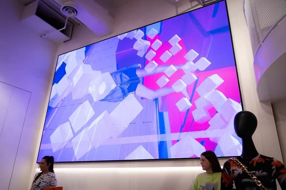 Large indoor LED screen in P.E Nation store displaying vibrant fashion visuals above mannequins and shoppers.