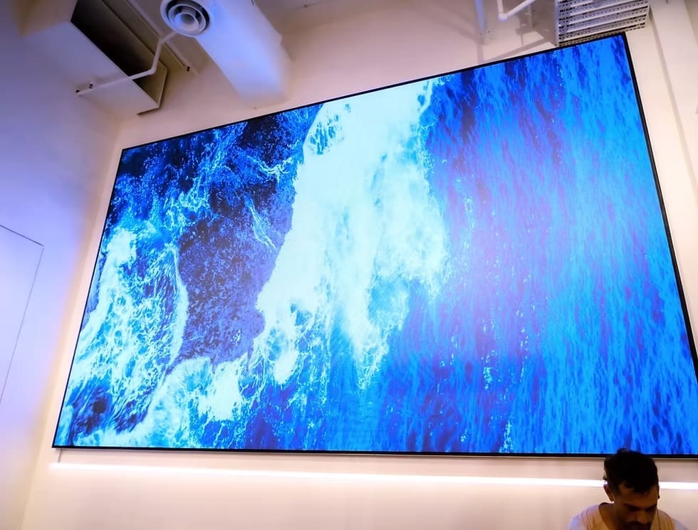 Large LED display in P.E Nation store showing high-resolution ocean wave visuals inside a modern retail environment.