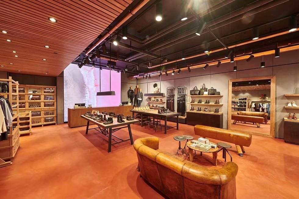 Interior of R.M. Williams store showcasing boots, apparel, and accessories with a digital LED wall display in the background.