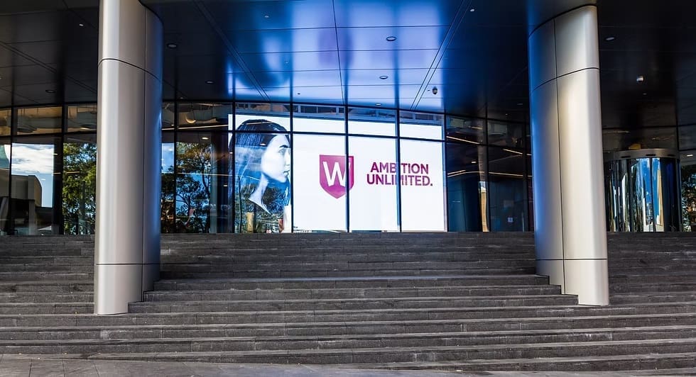 Wide view of Western Sydney University campus entrance with LED display showing “Ambition Unlimited” branding.